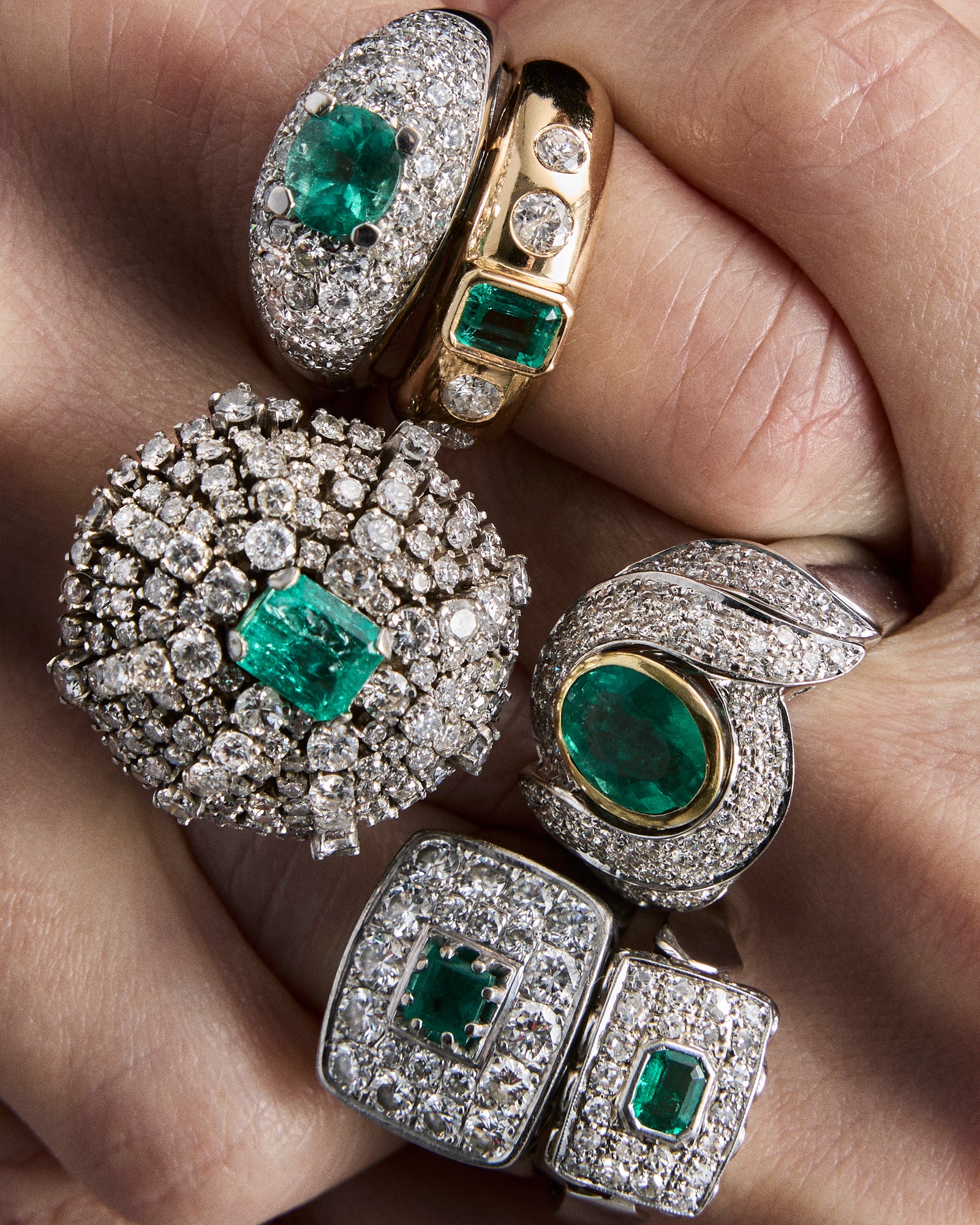 Close-up of multiple emerald and diamond rings on a hand.