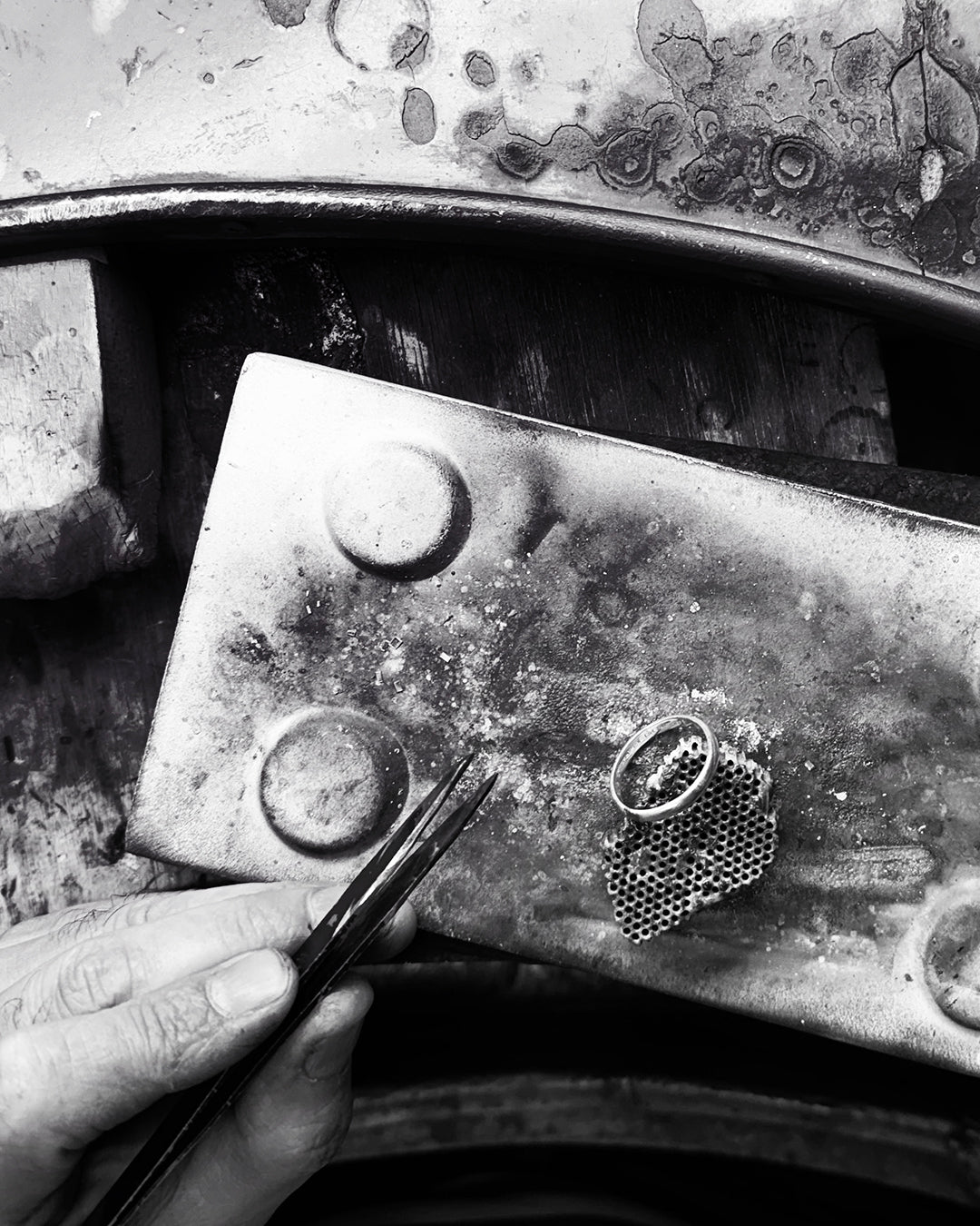 Close-up of a hand holding tweezers near a textured metal surface with a small honeycomb pattern.
