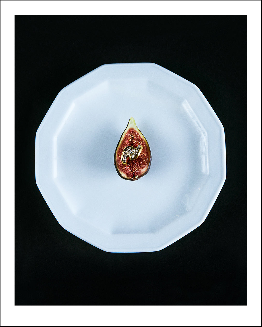 Halved fig on a white plate with a black background