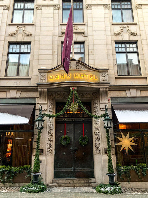 Bank Hotel entrance with decorative wreaths and a flag on a building facade.
